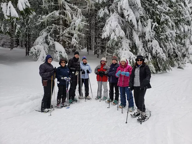 Group of people snowshoeing in a snowy forest.