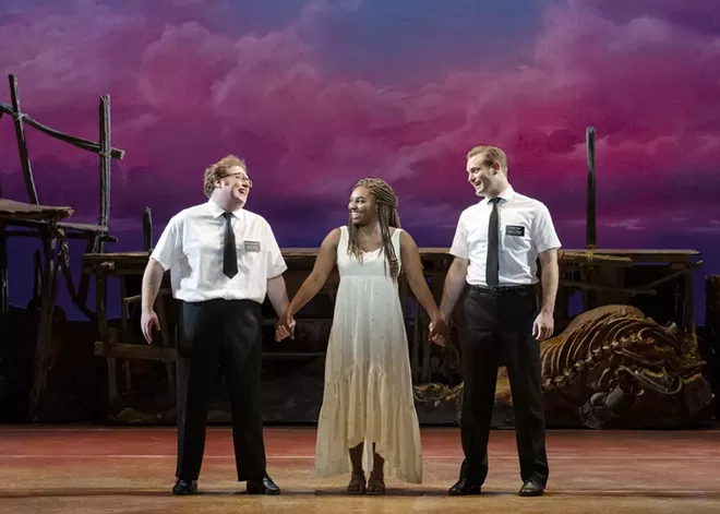 Actors portraying Elder Cunningham, Nabulungi and Elder Price stand on stage during a performance of Book of Mormon.